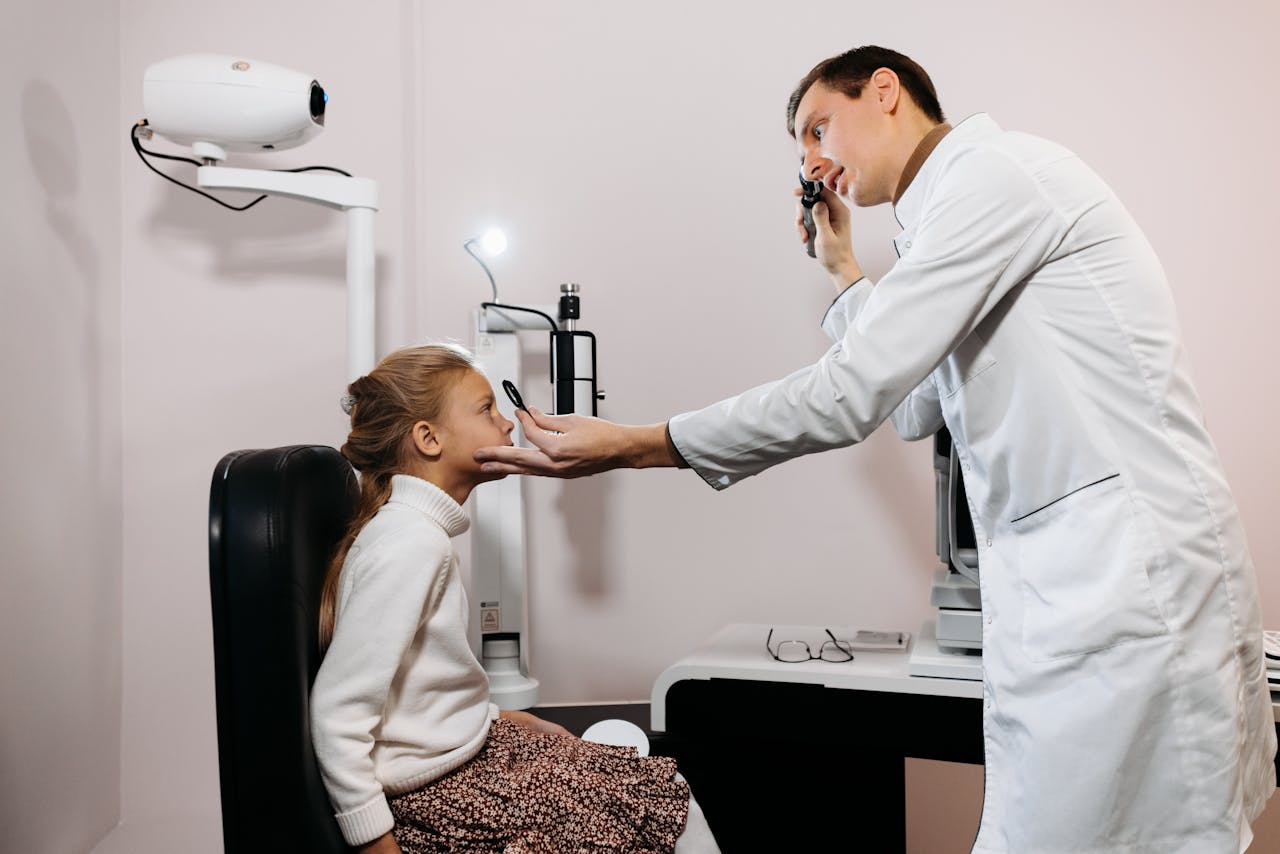 A medical professional performs an eye exam on a young girl in a clinic setting.